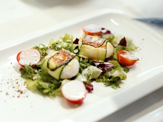 Cuisine at one of the top hotels in Grödnertal with 3 stars Fresh salad with grilled zucchini and tomatoes on white plate