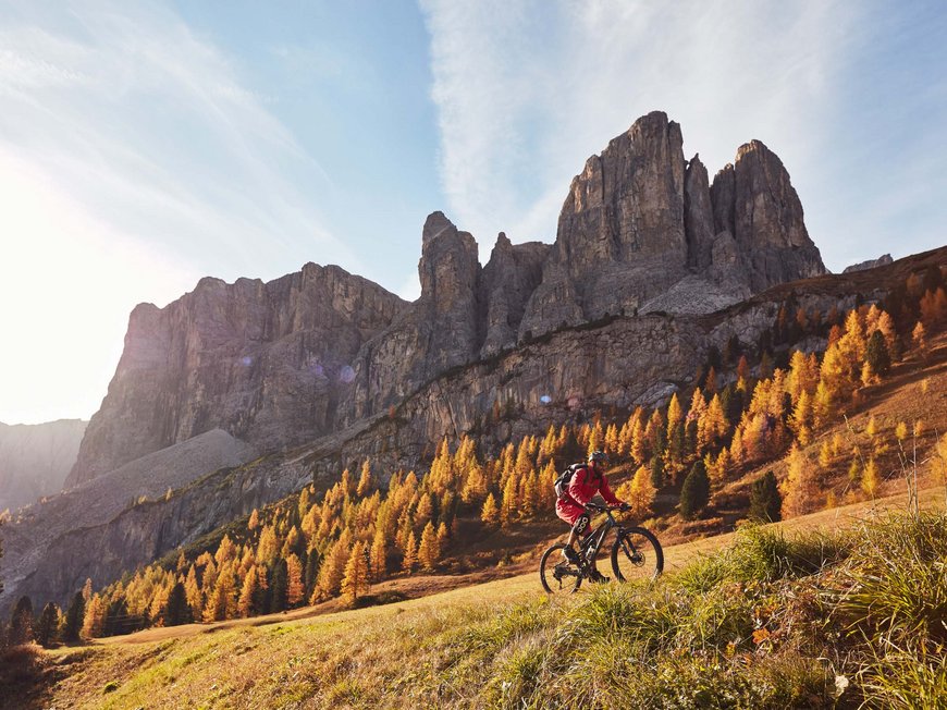 Dolomiten + Wandern + Hotel Cristallo = hallo Sommer! Mountainbiker fährt im Herbst vor einer felsigen Bergkulisse