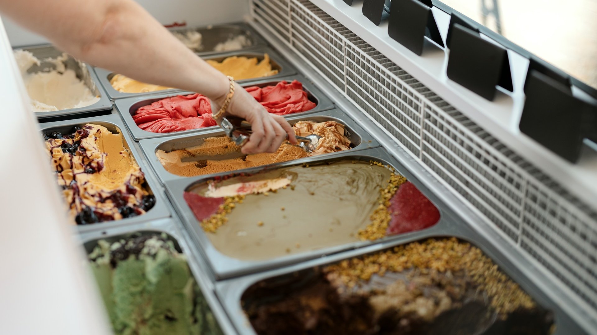 Inklusivleistungen deiner Gröden-Unterkunft Hand schöpft Eis aus einem Gefrierschrank mit verschiedenen Eissorten