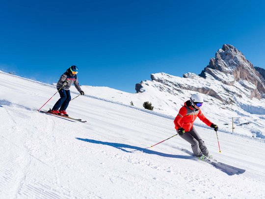 Vacanza in Val Gardena d’inverno Due sciatori scendono una pista innevata con montagne sullo sfondo