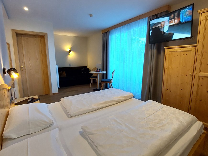 Deine Unterkunft in St. Christina im Grödnertal: Willkommen! Gemütliches Hotelzimmer mit Doppelbett, Holzschrank und Fernseher an der Wand