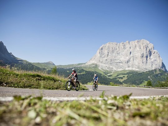 Dolomiten + Wandern + Hotel Cristallo = hallo Sommer! Zwei Radfahrer fahren auf Bergstraße mit großem felsigen Berg im Hintergrund