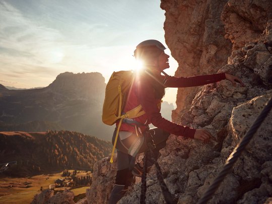 Dolomiten + Wandern + Hotel Cristallo = hallo Sommer! Frau klettert an felsigem Berg bei Sonnenuntergang mit Sicherheitsausrüstung
