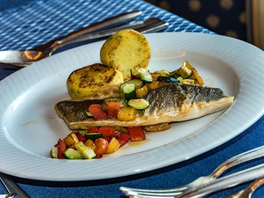 Deine Unterkunft in St. Christina im Grödnertal: Willkommen! Gebratener Fisch mit Gemüsewürfeln und zwei Kartoffelrouladen auf weißem Teller