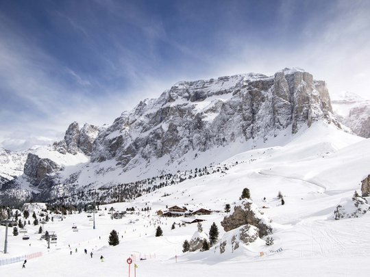 Vacanza in Val Gardena d’inverno Montagne innevate con pista da sci, sciatori e cielo blu