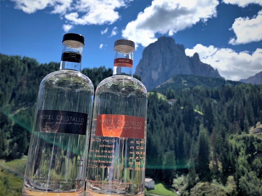 ECO-Sostenibilitá Due bottiglie di acqua Hotel Cristallo davanti a paesaggio montano e cielo blu