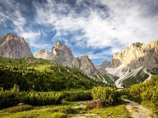 Dolomiten + Wandern + Hotel Cristallo = hallo Sommer! Grünes Tal mit Wanderweg vor hohen Felsen unter blauem Himmel