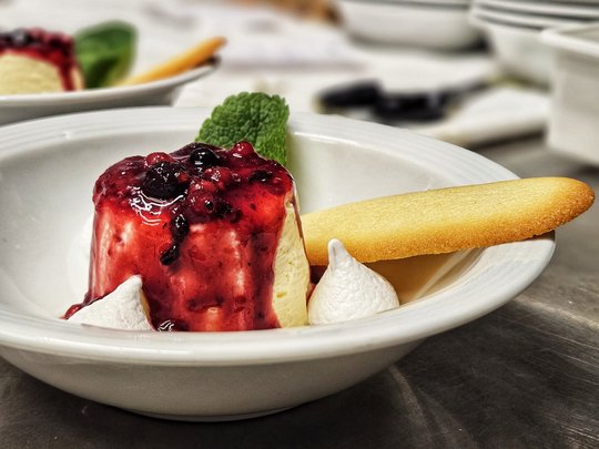 Cuisine at one of the top hotels in Grödnertal with 3 stars Dessert with berry sauce, mint leaf, meringue, and cookie on white plate