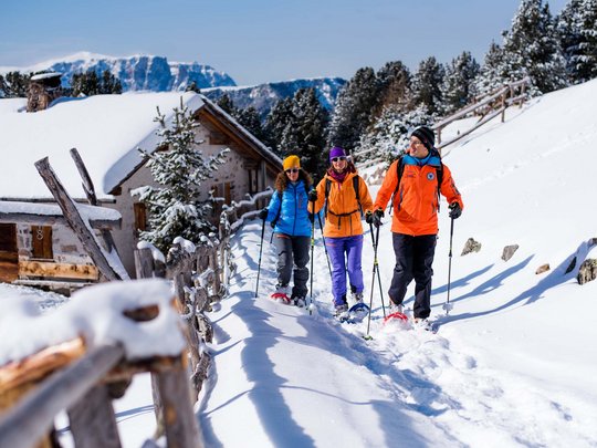 Vacanza in Val Gardena d’inverno Tre persone che fanno escursioni con ciaspole su un sentiero innevato