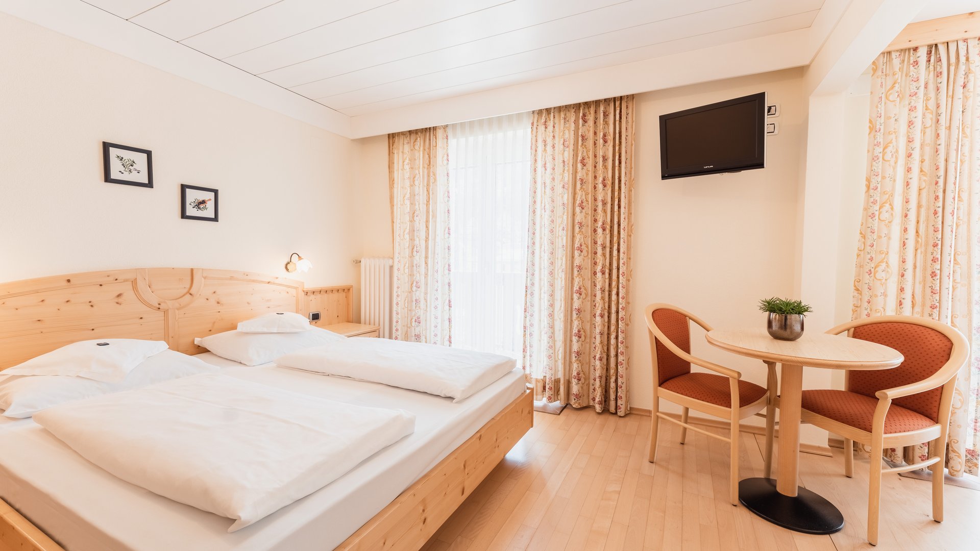 Hotel a Santa Cristina, Val Gardena, con mezza pensione Camera d'albergo accogliente con letto matrimoniale, tavolo, sedie e televisore