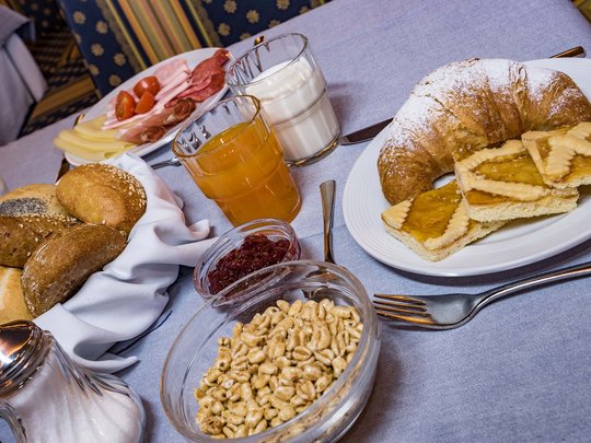 Cuisine at one of the top hotels in Grödnertal with 3 stars Breakfast table with bread rolls, croissant, cold cuts, cereal, juice, and milk