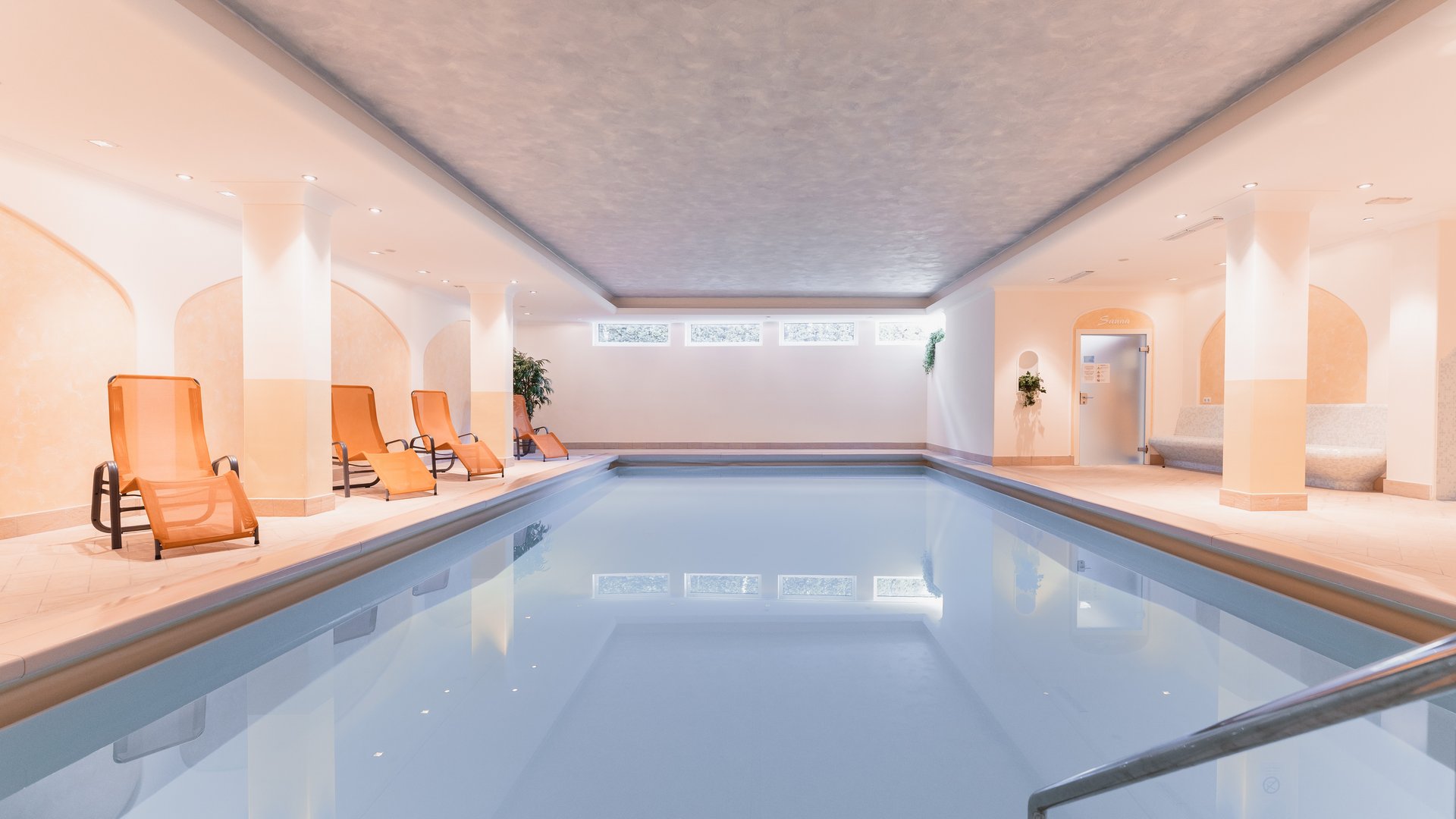 Südtirol-Hotel mit Pool (3 Sterne) gesucht? Hier ist es! Helles Innenhallenbad mit orangen Liegestühlen und Sauna