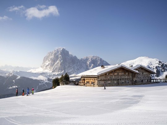 Vacanza in Val Gardena d’inverno Sciatori davanti a una baita in alta montagna innevata con cielo sereno