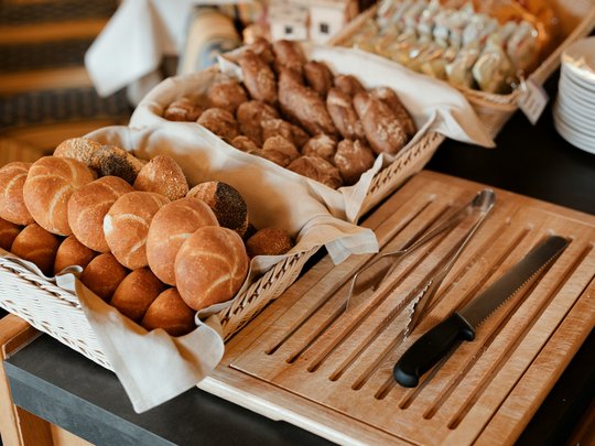 Cuisine at one of the top hotels in Grödnertal with 3 stars Assorted fresh bread rolls in basket with bread knife and tongs on wooden board