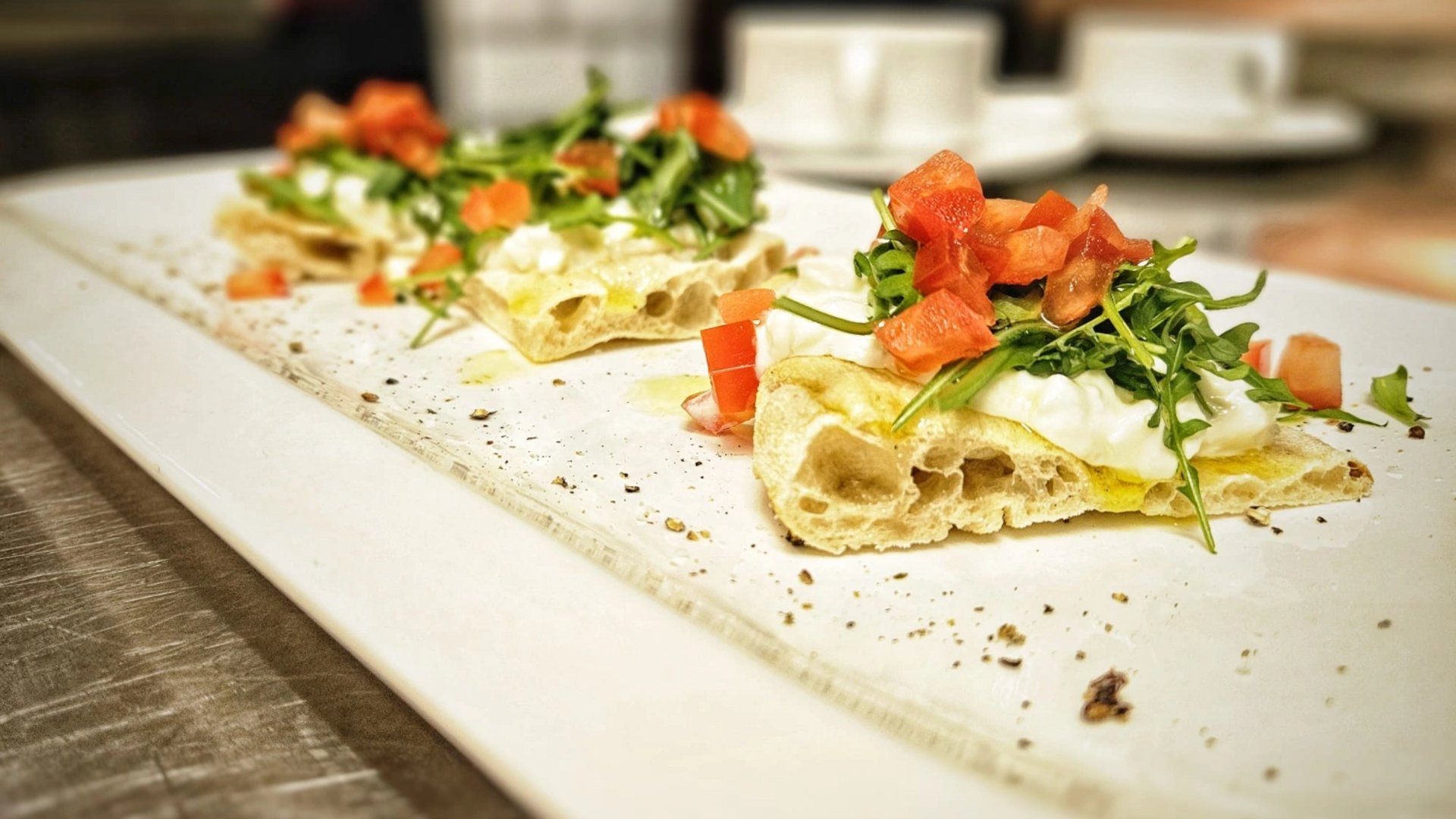 Cuisine at one of the top hotels in Grödnertal with 3 stars Three pizza slices with arugula, cream cheese, and tomato on a white plate