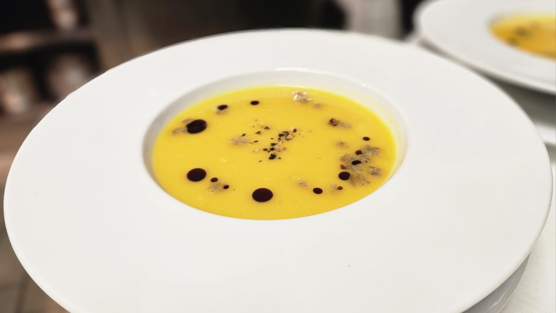 Cuisine at one of the top hotels in Grödnertal with 3 stars Pumpkin soup in white bowl with decorative drops and spices