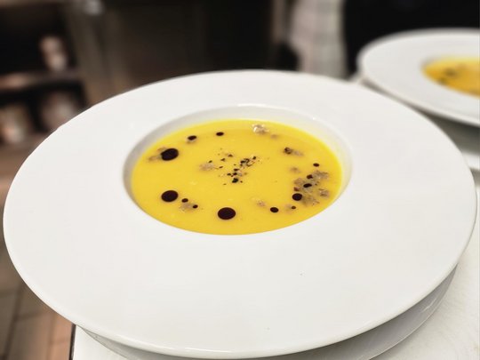 Cuisine at one of the top hotels in Grödnertal with 3 stars Pumpkin soup in white bowl with decorative drops and spices