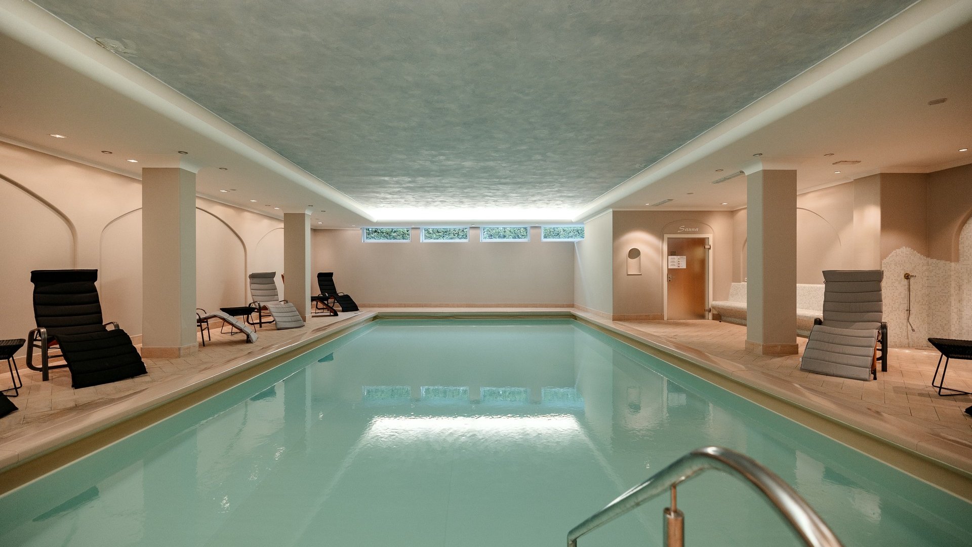 Inclusive services at your Gröden accommodation Modern indoor pool with lounge chairs and sauna in the background