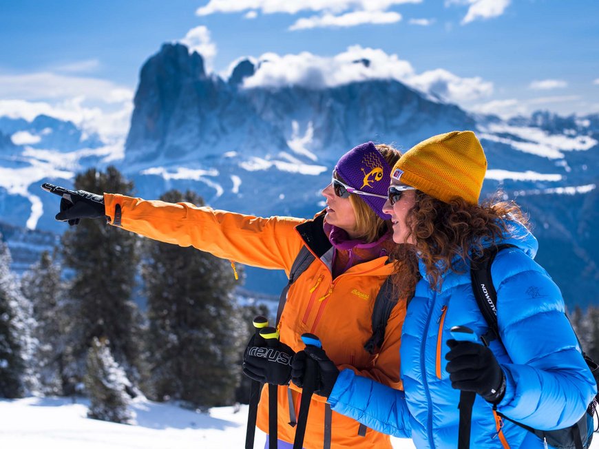 Vacanza in Val Gardena d’inverno Due donne con abbigliamento invernale indicano montagne innevate sullo sfondo