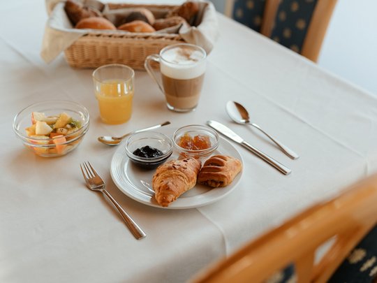 Cuisine at one of the top hotels in Grödnertal with 3 stars Breakfast with croissants, jam, fruit salad, and drinks on white tablecloth