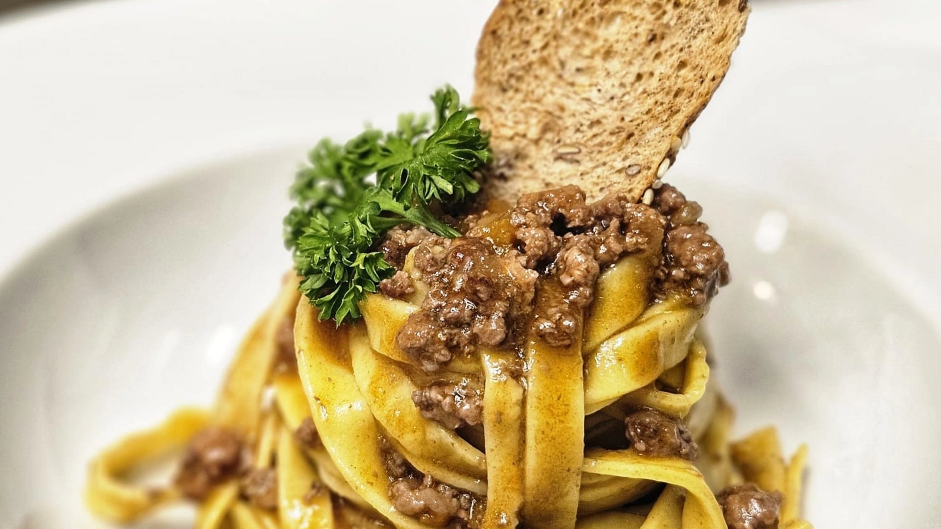 Cuisine at one of the top hotels in Grödnertal with 3 stars Pasta with ground meat sauce, parsley, and toasted bread slice on white plate