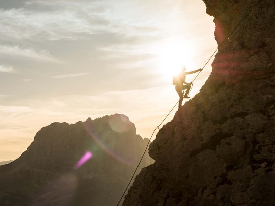 Dolomiten + Wandern + Hotel Cristallo = hallo Sommer! Kletterer steigt bei Sonnenlicht an steiler Felswand im Gebirge auf