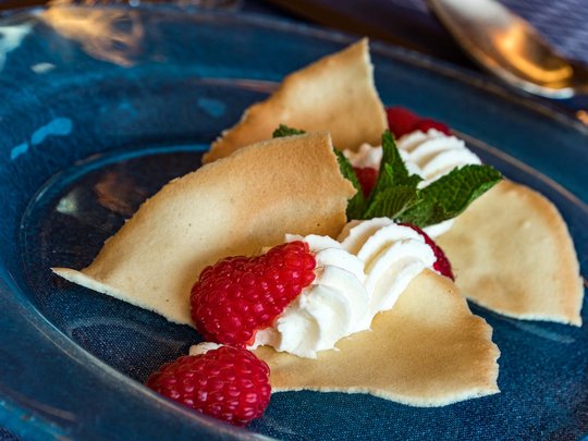 Cuisine at one of the top hotels in Grödnertal with 3 stars Sweet dessert with raspberries, whipped cream, and thin crispy cookies on blue plate