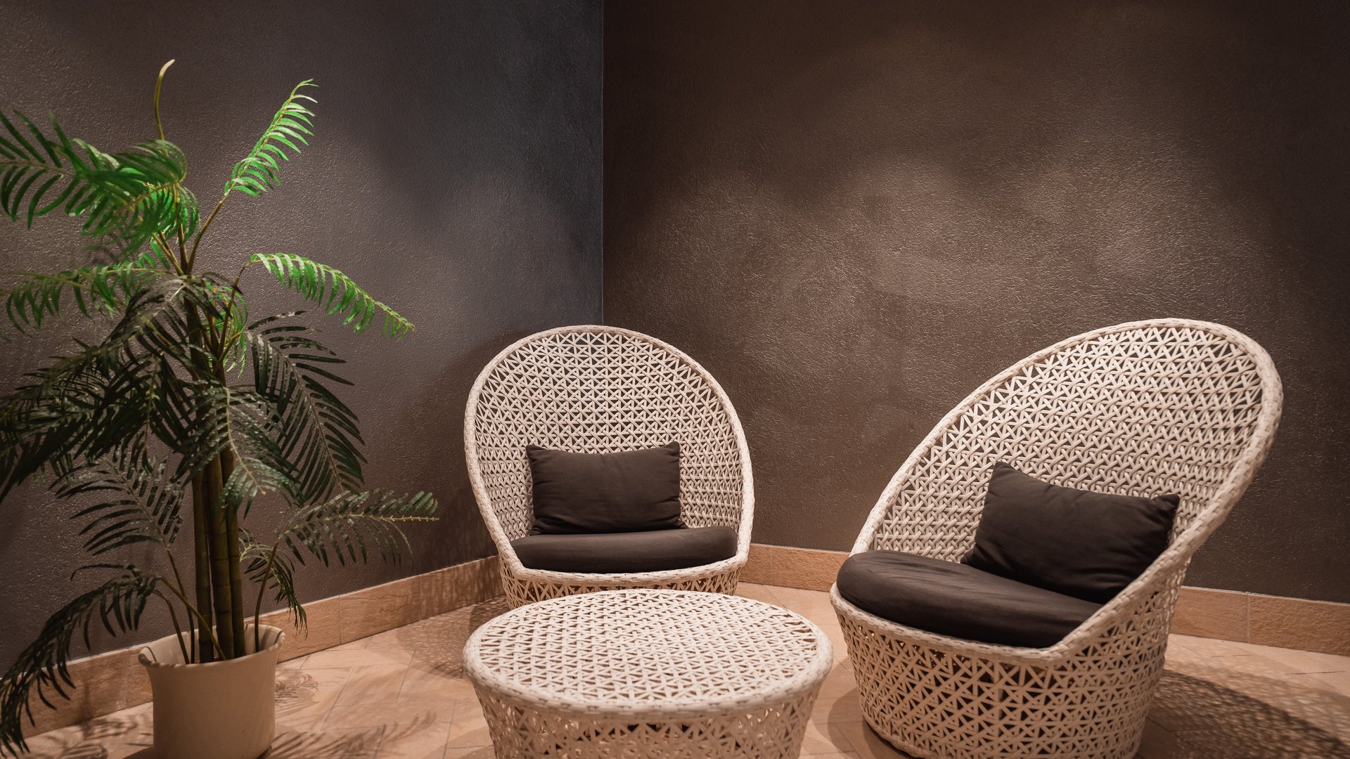 Südtirol-Hotel mit Pool (3 Sterne) gesucht? Hier ist es! Weißes Rattanmöbel-Set mit zwei Sesseln und einem Tisch in dunklem Raum