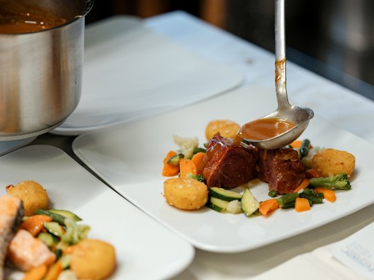 Cuisine at one of the top hotels in Grödnertal with 3 stars Sauce being poured on roasted meat with vegetables and croquettes on white plate