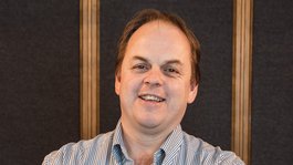 Your hosts in the Dolomites. Hotels + 3 stars? Cristallo! Man smiling with arms crossed in front of dark background