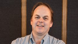 Die Gastgeber deines Dolomiten-Hotels (3 Sterne) Mann lächelnd mit verschränkten Armen vor dunklem Hintergrund