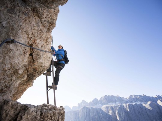 Dolomiten + Wandern + Hotel Cristallo = hallo Sommer! Kletterer steigt eine Leiter an einer Felswand mit Bergpanorama