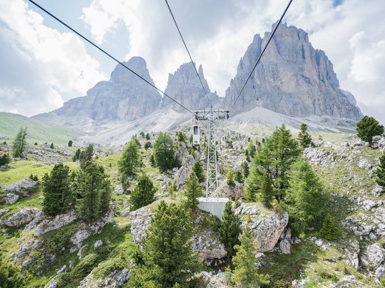 Dolomiten + Wandern + Hotel Cristallo = hallo Sommer! Seilbahn über grünes Gebirgstal mit Felsbergen im Hintergrund