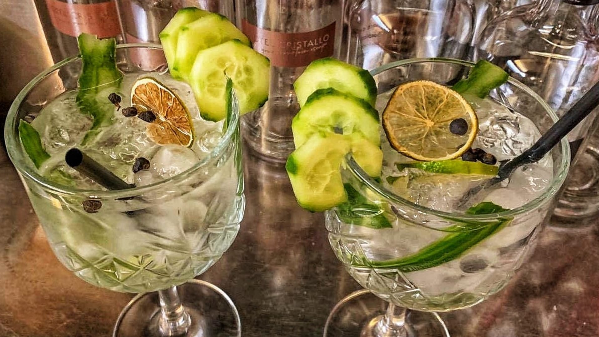 La tua vacanza in Val Gardena è qui Due cocktail con fette di cetriolo e limone su un tavolo con bottiglie sullo sfondo