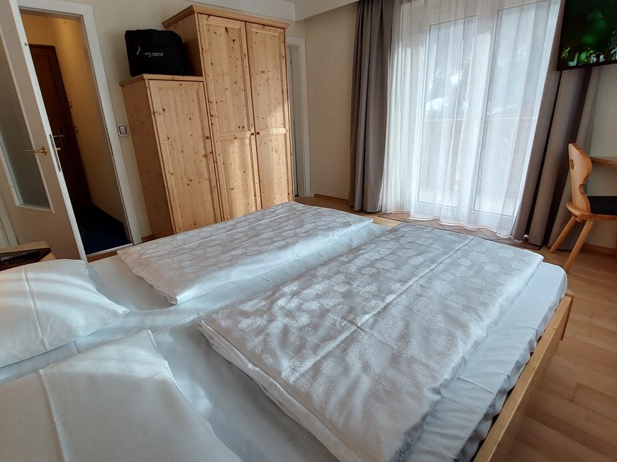 Hotel a Santa Cristina, Val Gardena, con mezza pensione Camera d'albergo accogliente con letto matrimoniale, armadio in legno e balcone con tende