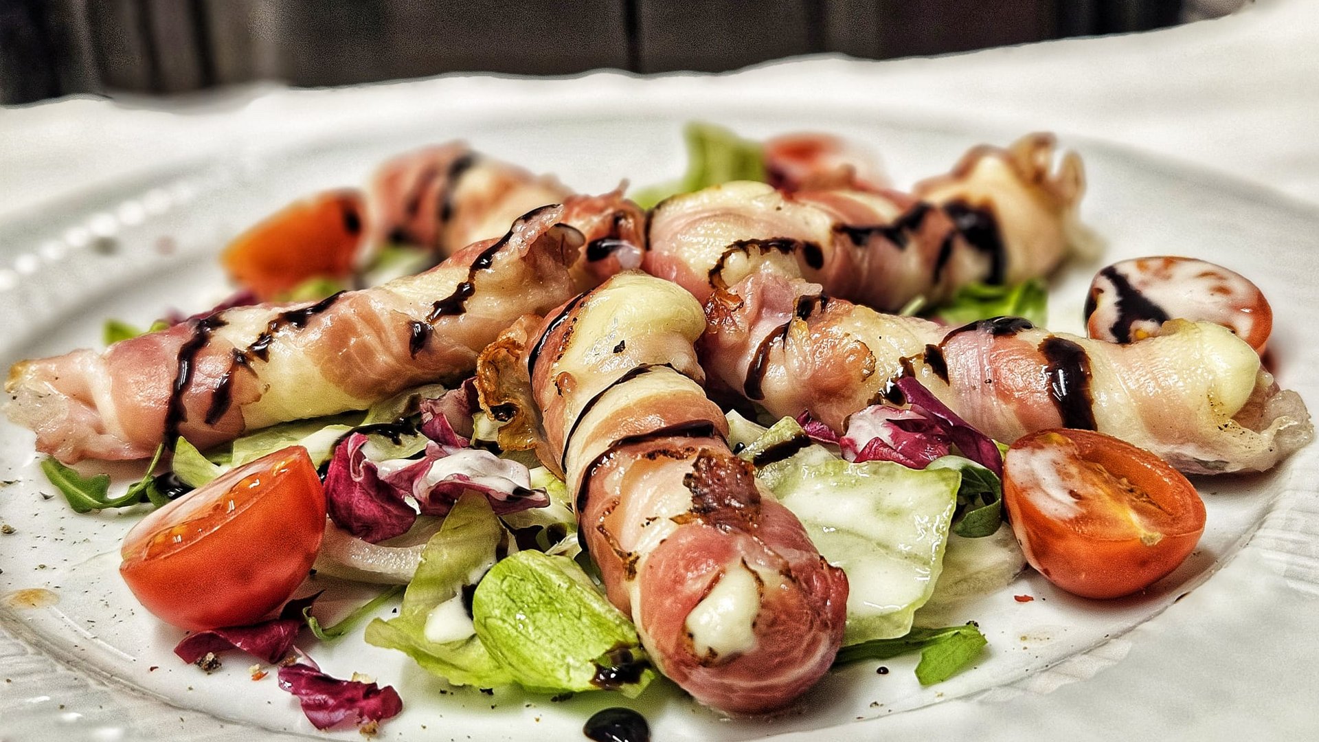 Cuisine at one of the top hotels in Grödnertal with 3 stars Cheese rolls wrapped in bacon on salad with tomatoes and balsamic drizzle