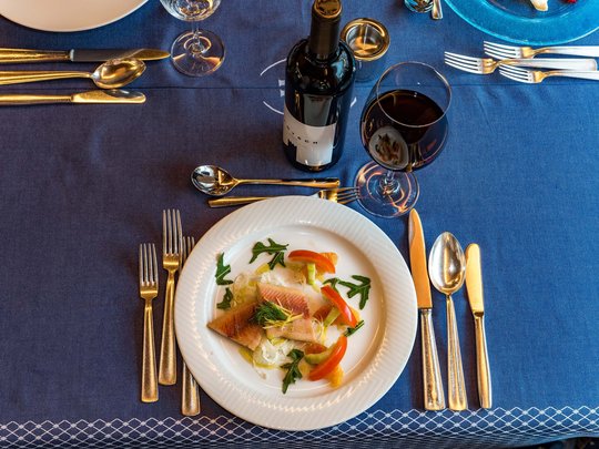 Cuisine at one of the top hotels in Grödnertal with 3 stars Table setting with fish dish, red wine glass, and cutlery on blue tablecloth