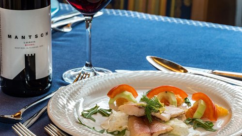 Hotel Cristallo: experience the Dolomites with these extras Dish with fish fillet, vegetables and orange slices on white plate, glass of red wine beside