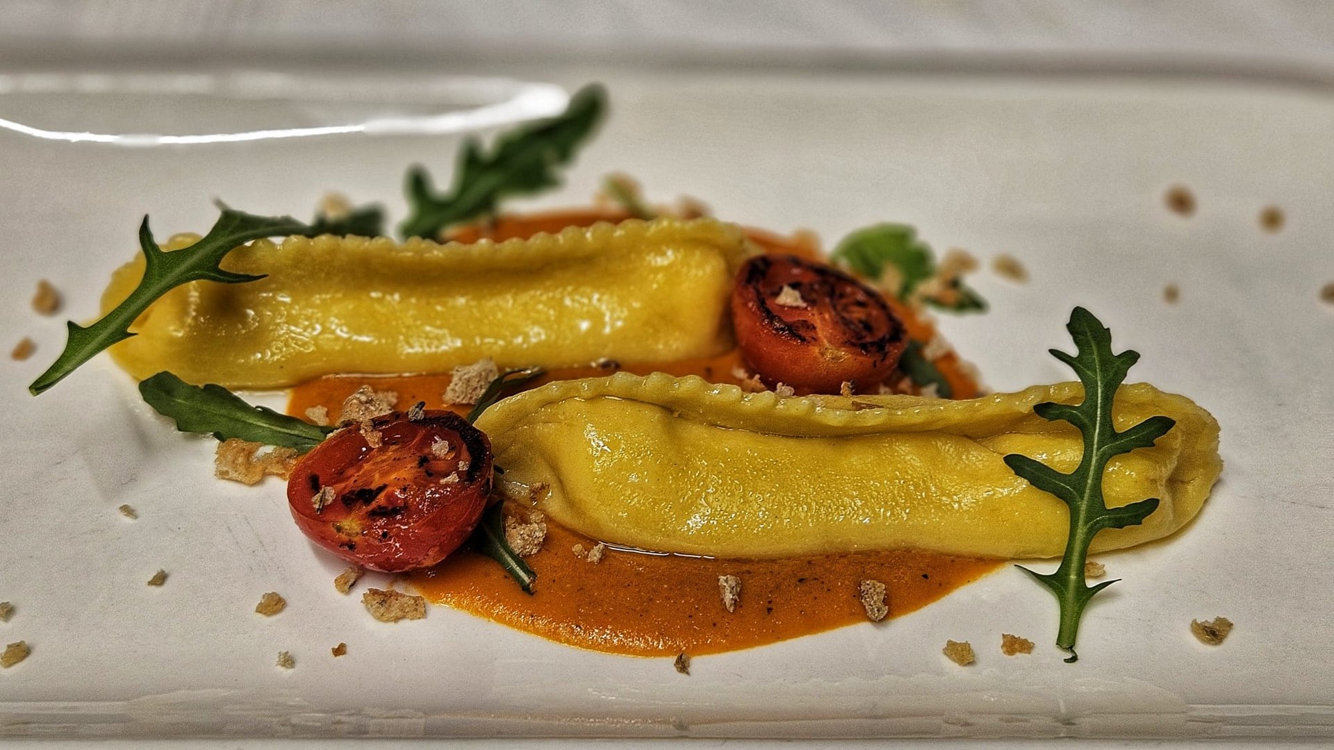 Cuisine at one of the top hotels in Grödnertal with 3 stars Two ravioli on sauce with grilled tomato and arugula on white plate