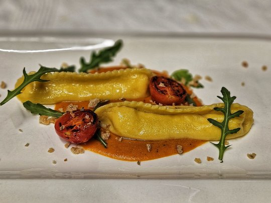 Cuisine at one of the top hotels in Grödnertal with 3 stars Two ravioli on sauce with grilled tomato and arugula on white plate