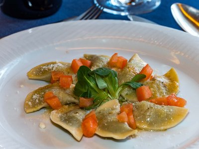 Deine Unterkunft in St. Christina im Grödnertal: Willkommen! Teller mit Ravioli, garniert mit Tomatenwürfeln und grünem Blattgemüse